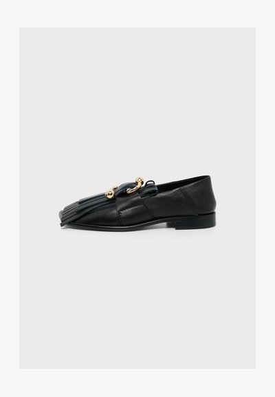 Mocassin en cuir noir avec détail à franges sur le devant et accents dorés en forme de boule et d'anneau, semelle plate et petit talon.