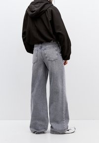 Giacca leggera nera con cappuccio abbinata a jeans in denim grigi, a vita alta e dal taglio morbido, con tasche posteriori e orli grezzi.