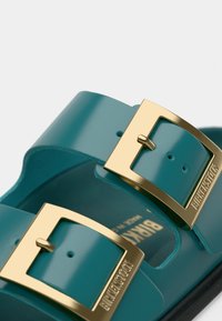 Τιρκουάζ σανδάλια με δύο ρυθμιζόμενα λουριά, χρυσά αγκράφες, κατασκευασμένα από λείο, γυαλιστερό υλικό. Διαθέτουν σχηματισμένο πέλμα και τυπωμένο λογότυπο της μάρκας.