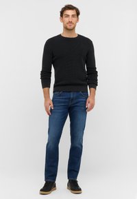 Maglione nero a coste con maniche lunghe e collo rotondo abbinato a jeans blu a gamba dritta e sneakers nere. Look casual con tessuto testurizzato.