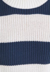 Pull en maille présentant des rayures alternées épaisses bleu marine et blanc, avec une texture côtelée et un large col rond.