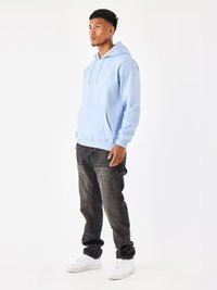 Felpa con cappuccio azzurro chiaro, dotata di tasca frontale e dettaglio grafico. Abbinata a jeans di denim scuri e sneaker bianche.