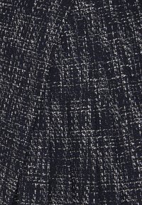 Tissu tweed tissé bleu foncé et blanc avec un motif texturé en forme de grille et des fils entrelacés visibles.