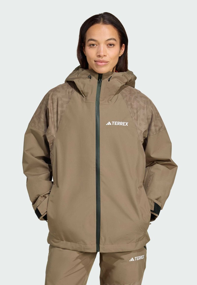 Light brown waterproof jacket with a hood and ribbed fabric accents on shoulders. Features zipper closure and logo on chest.