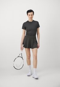 Conjunto deportivo que incluye una camiseta ajustada gris oscuro y una falda pantalón, con una textura suave, combinado con calcetines blancos y zapatillas, sosteniendo una raqueta de tenis.