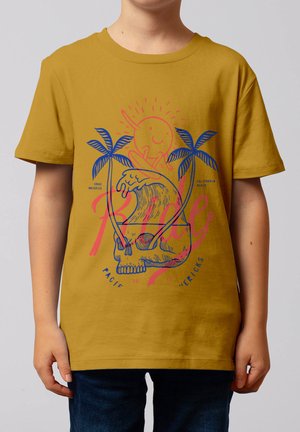 Kind trägt senfgelbes T-Shirt mit Grafik von Schädel, Palmen, Meereswelle und Sonne und hält ein Surfbrett.