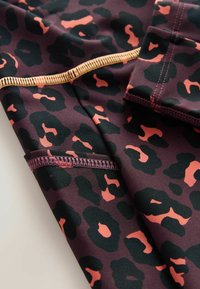 Leopardų rašto audinys tamsiai raudoname ir juodame fone su koraliniais akcentais. Pasižymi lygiomis siūlėmis ir glotniai, elastinga tekstūra.