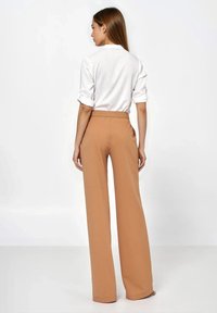 Brązowe spodnie o szerokich nogawkach o gładkiej fakturze i elastycznym pasie, w połączeniu z białą koszulą z podwiniętymi rękawami.