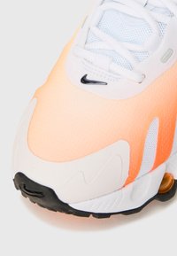 Tenisky Nike so stredným odtieňom oranžovej a bielej na vrchnej časti, sieťovinovými panelmi, čiernymi akcentmi a výrazným textúrovaným špičkou.