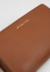Portafoglio in pelle marrone con texture, con il logo in oro "MICHAEL KORS" impresso nell'angolo e cuciture visibili lungo i bordi.