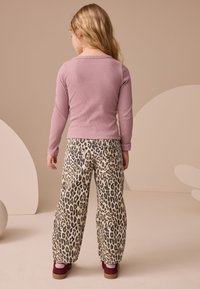 Top mov deschis cu mâneci lungi și textură nervurată, asortat cu pantaloni largi bej cu imprimeu leopard și pantofi roșu închis cu talpă platformă.