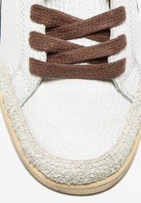 Sneaker bianco in pelle con lacci intrecciati marroni, rifiniture in suede grigio testurizzato e suola in gomma crema, caratterizzata da dettagli di cucitura sottili.