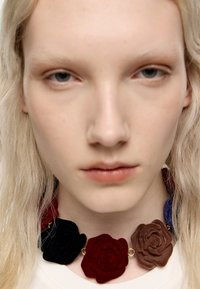 Naszyjnik kwiatowy z elementami filcowej róży w kolorach czerwonym, czarnym, brązowym i niebieskim, połączony złotym metalem. Gładka faktura z warstwowym wzornictwem.