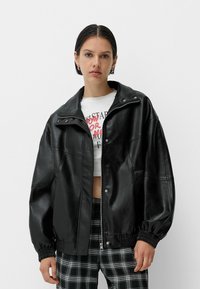 Jachetă din piele sintetică neagră cu o croială relaxată, guler cu capse, manșete elastice și textură netedă. Purtați-o peste un tricou alb scurt cu grafică.