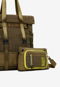 Grüne, gewebte Tragetasche mit strukturiertem Finish, ausgestattet mit orangenen Trageriemen und einem kleineren, passenden Crossbody-Beutel mit einem gelben Akzent.