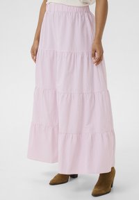 Jupe maxi à volants rayée rose et blanche avec une taille élastique, en tissu fluide et avec une coupe décontractée, associée à des bottines à talons marron.