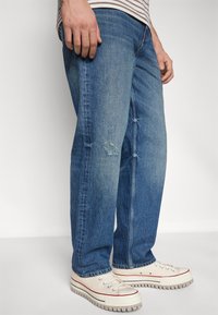 Blugi din denim albastru estompat, cu o croială relaxată, având detalii uzate la genunchi. Asortați cu adidași crema și o cămașă stripată.