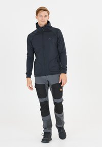 Svart zip-up huvajacka med sidofickor, tillsammans med grå cargobyxor med svarta detaljer och knäpatchar. Båda är gjorda av stretchigt material.