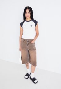 Hvid og marineblå raglan T-shirt med et kaktusmotiv, brune denim shorts, hvide sokker og sorte klipklapper. Glat, afslappet outfit.