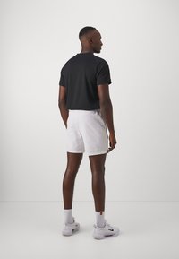 Zwarte T-shirt met korte mouwen gecombineerd met witte shorts. De outfit heeft een eenvoudig ontwerp, met een gladde stof en geen zichtbare patronen of accenten.