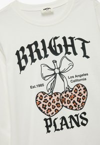 Hvid bomulds T-shirt med et grafisk design af to lyserøde leopardmønstret hjerter bundet med en sort sløjfe, teksten siger "BRIGHT PLANS Los Angeles Est. 1985."