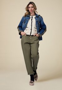 Jeansjacke mit kontrastierenden Ärmeln, gestrickter cremefarbener Pullover mit schwarzen Akzenten, olivgrüne weit geschnittene Hose und hellpinkfarbene Sandalen mit Riemchen.