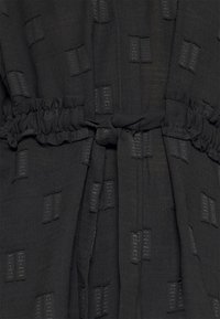Tissu noir avec un motif texturé de formes rectangulaires, rassemblé à la taille avec un lien assorti pour la forme et l'ajustement.