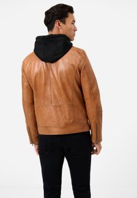 Hellbraune Lederjacke mit schwarzer Kapuze, mit tailliertem Schnitt, seitlichen Reißverschlüssen und glatter Textur. Sichtbare Nahtdetails auf dem Rücken.
