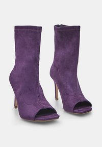 Violet nubuck korkokengät, joissa on avoimet varpaat ja sivuvetoketjut, esillä valkoisella taustalla.