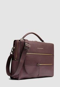 Dunkelbraune Lederaktentasche mit zwei vorderen Reißverschlusstaschen, Tragegriff oben und verstellbarem Schulterriemen vor einfarbig hellem Hintergrund.