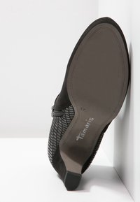 Zapato de ante negro con parte superior de malla texturizada, cremallera lateral y suela de goma. Presenta el nombre de la marca "Tamaris" y el tamaño 37 en la suela.