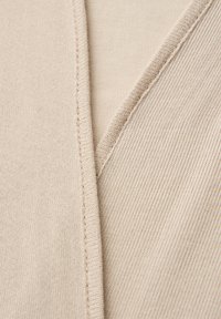 Gros plan sur un tissu en maille beige montrant un col en V avec un fin côtelé et des coutures visibles le long de la couture.