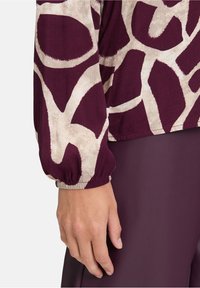Maglietta a maniche lunghe in bordeaux e crema con un motivo astratto, bordi delle maniche arricciati e una texture di tessuto morbido. Abbinata a pantaloni coordinati.