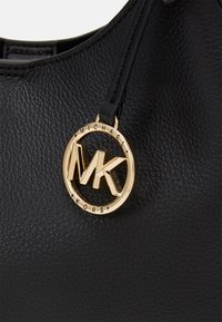 Sac en cuir texturé noir avec un pendentif rond doré du logo Michael Kors suspendu à une fine bandoulière en cuir.