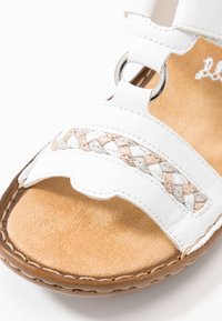 Sandale en cuir blanc avec un accent tissé et des détails en métal circulaire argenté, dotée d'une semelle intérieure en suède tan doux et de détails à bords festonn�és.