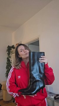 Svart stövel upp till knät med spetsig tå och polerat läder, utrustad med stilettklack och minimala söm-detaljer.