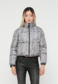 Padded bomber jacket in gray with a black and white leopard print. Features a high collar and zip closure. Worn with black pants.