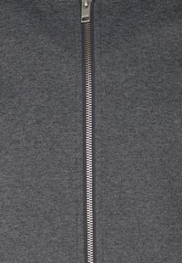 Grå zipjacka av texturerat tyg med en central metallblixtlås med silverfärgade tänder och en stående krage.