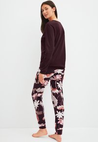 Ensemble de vêtements d'intérieur confortable comprenant un haut bordeaux à manches longues et un pantalon noir orné de motifs floraux en rose et blanc.