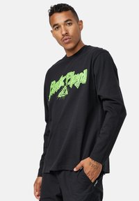 Sort langærmet t-shirt med et grønt grafisk print af teksten "Pink Floyd" og et øje-symbol, lavet af bomuldsstof.