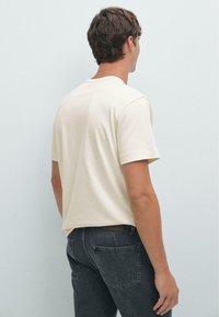 Beige katoenen T-shirt met korte mouwen, een losse pasvorm en een ronde hals, gecombineerd met donkergrijze denim jeans voorzien van achterzakken.