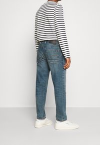 Jeansy dżinsowe w średnim odcieniu, luźnego kroju, z widocznymi przeszyciami na kieszeniach. Połączone z czarno-białą koszulką w paski z długim rękawem oraz białymi tenisówkami.