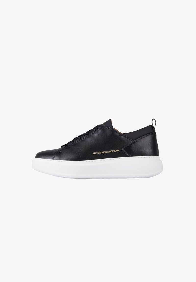 Sneaker nero low-top con suola bianca spessa, lacci neri, linguetta sul tallone e logo dorato "Alexander Smith" sul lato.