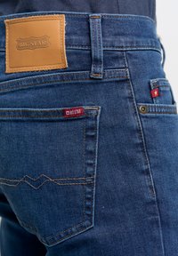 Sinine teksapükste lähedalt võetud pilt, kus on pruunast nahast "BIG STAR" silt ja tasku ääres punane kangast silt.