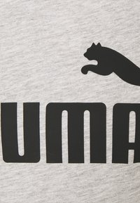 Grått tyg med djärv svart text som stavar "PUMA" med en hoppande panter-silhuett ovanför texten. Slät textur, avslappnad design.