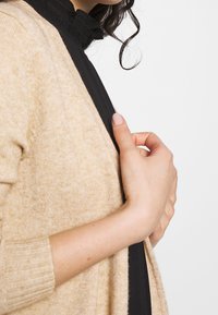 Beige och svart cardigan med en mjuk textur, öppen front och ribbade manschetter. Designen inkluderar kontrastpaneler och en avslappnad passform.