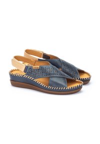 Sandalias de cuero con una parte superior azul oscuro que presenta diseños florales troquelados y acentos beige. Con detalles de borde cosido y una suela acolchada.