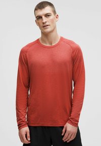 Tricou sport texturat cu mâneci lungi, de culoare roșie, cu decolteu rotund și manșete strânse, asortat cu pantaloni scurți negri.