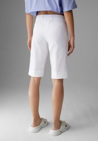 Bílé krátké kalhoty na míru s rovnými nohavicemi, vyhrnutými lemy a hladkou texturou. Nošeny s lehkými světlými sandály na volný čas.