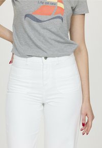 T-shirt gris à manches courtes avec un motif de bateau à voile en orange et bleu, associé à un jean en denim blanc taille haute avec des poches avant.